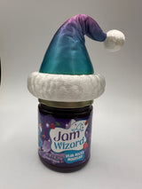 A jar of Jam Wizard Rocky Mountain Jam with a festive Santa hat decoration in the color of Mountain Mirage on the lid, photographed against a plain light gray background.